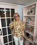 A woman  wearing the Tiffany blouse  with a brown and tan leaf pattern and white pants.