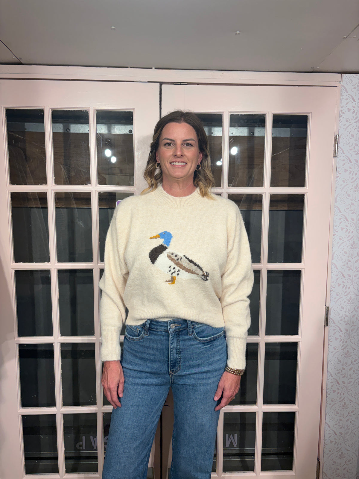 A woman wearing The Layla Sweater crafted from soft heathered knit fabric, features a relaxed fit ,crew neckline and long sleeves with a duck intarsia graphic at the front 