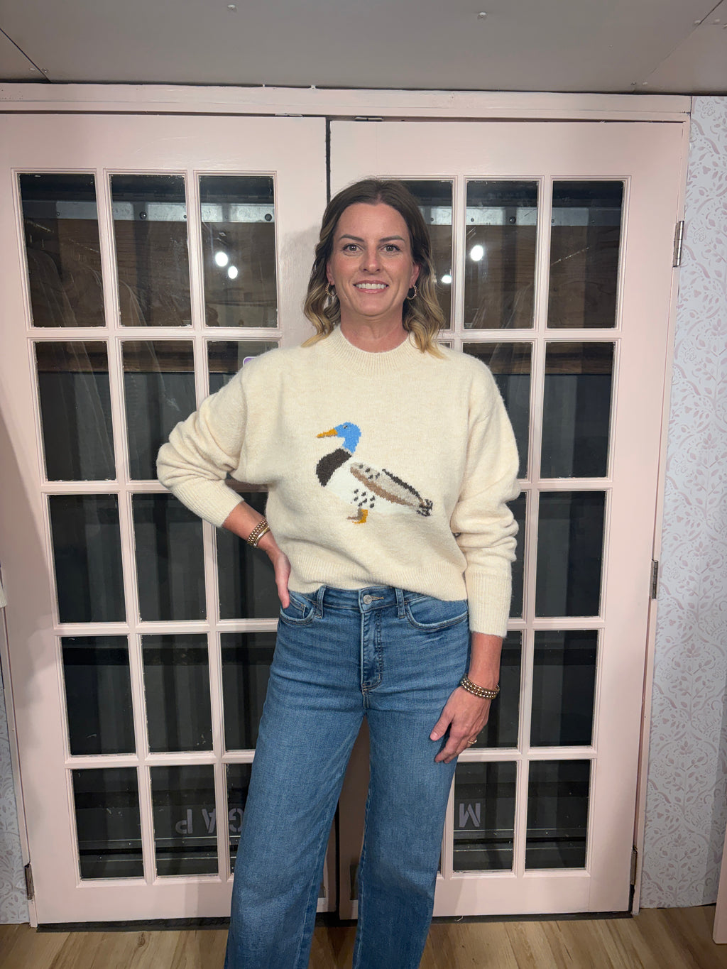 A woman wearing The Layla Sweater crafted from soft heathered knit fabric, features a relaxed fit ,crew neckline and long sleeves with a duck intarsia graphic at the front 