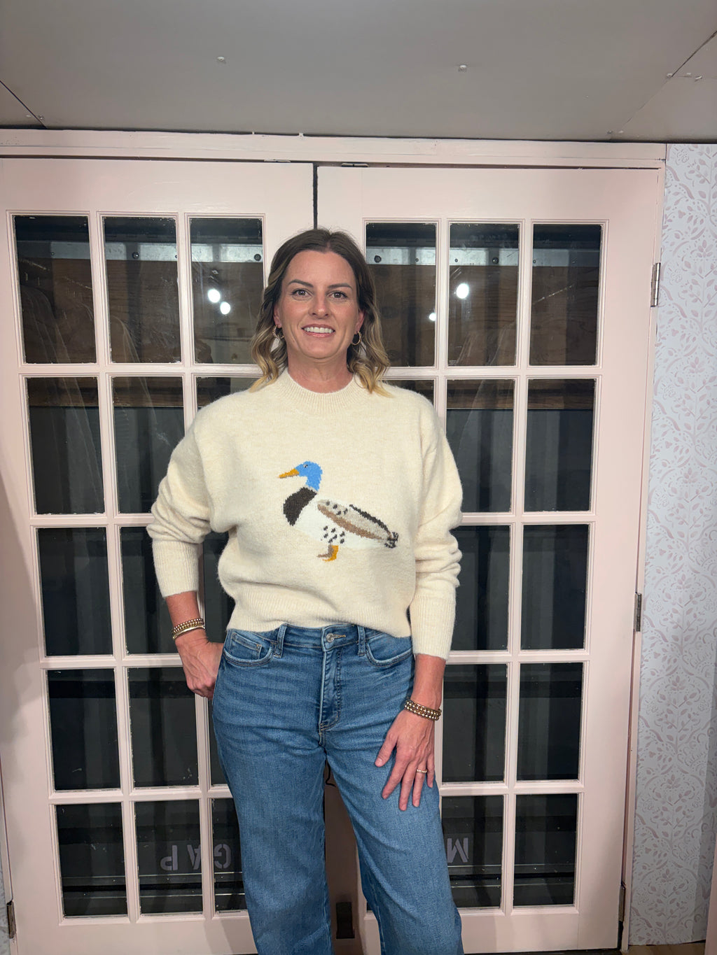 A woman wearing The Layla Sweater crafted from soft heathered knit fabric, features a relaxed fit ,crew neckline and long sleeves with a duck intarsia graphic at the front 