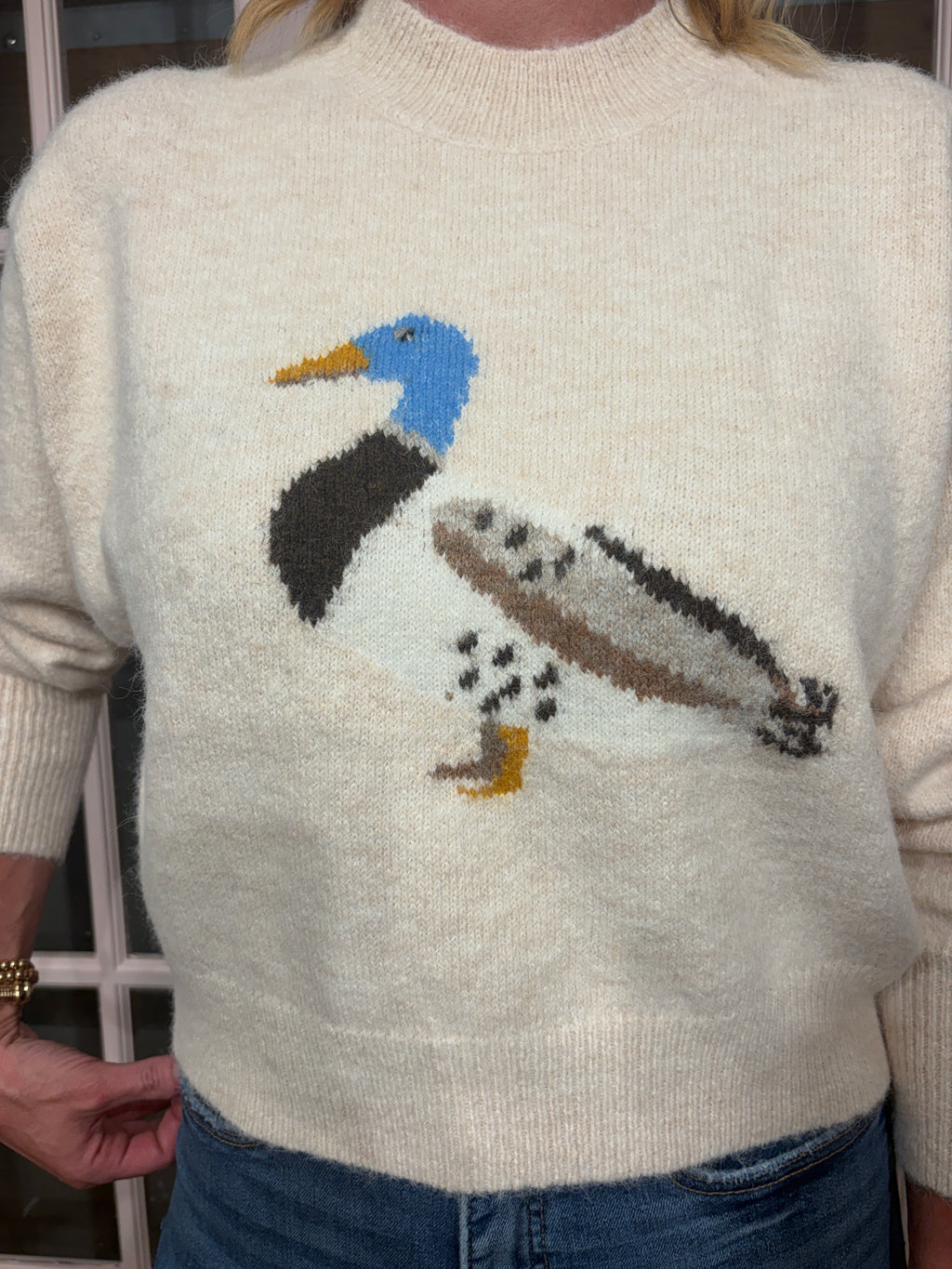 A woman wearing The Layla Sweater crafted from soft heathered knit fabric, features a relaxed fit ,crew neckline and long sleeves with a duck intarsia graphic at the front 