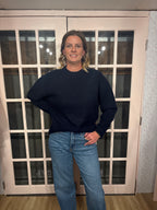 A woman wearing The Lennon Sweater that is a relaxed knit sweater with a soft brushed marled texture and crew neckline. Long sleeves, dropped shoulders, and wide ribbed trim at the cuffs and hem