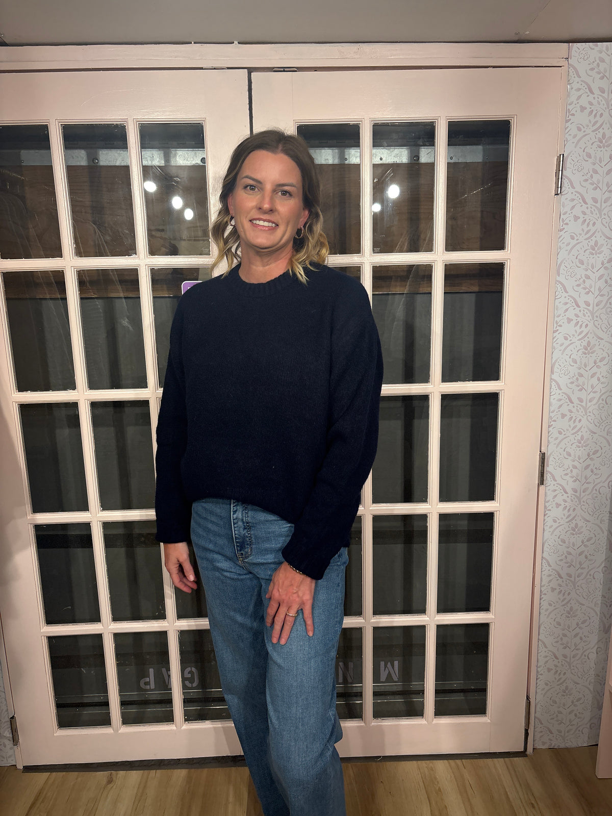 A woman wearing The Lennon Sweater that is a relaxed knit sweater with a soft brushed marled texture and crew neckline. Long sleeves, dropped shoulders, and wide ribbed trim at the cuffs and hem