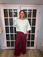 A woman wearing the Denise Pants in burgundy with a flattering high rise fit and a relaxed wide leg silhouette