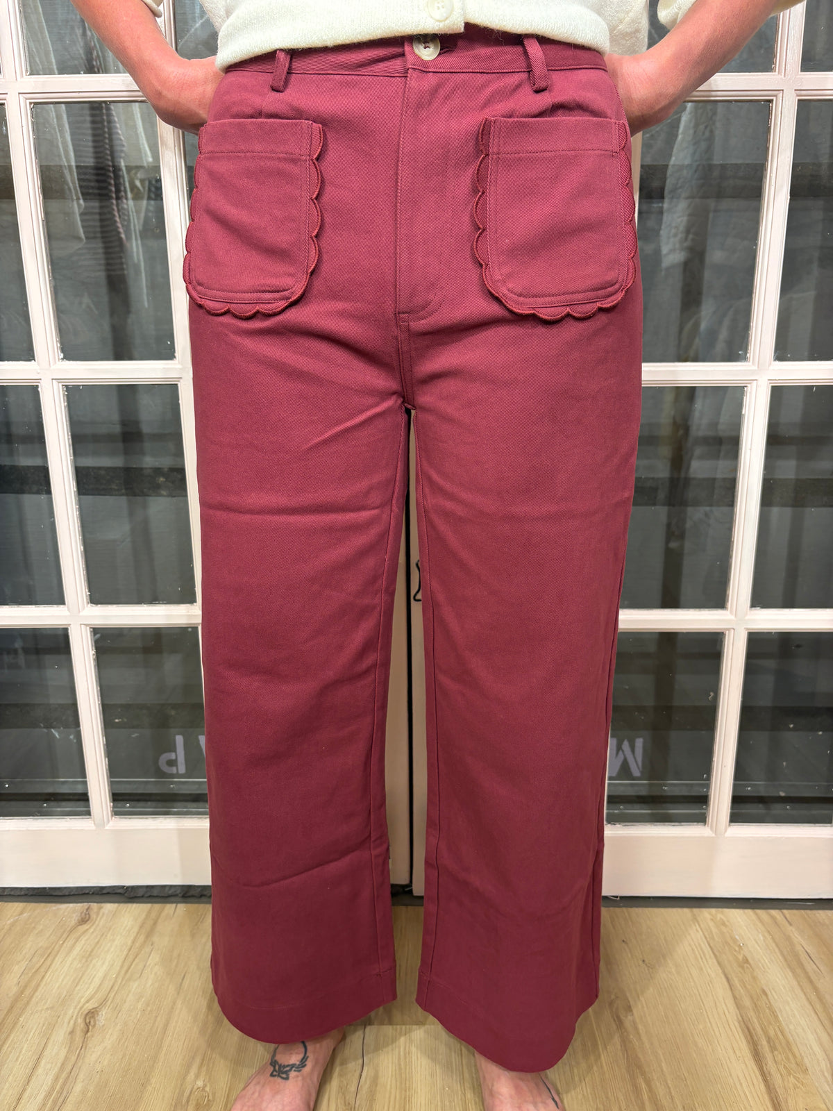 A woman wearing the Denise Pants in burgundy with a flattering high rise fit and a relaxed wide leg silhouette