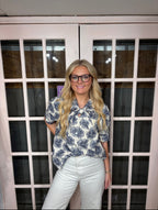 A woman wearing the Dawn Blouse Featuring a floral jacquard woven fabric, puff shoulders, a classic button-down front, and a delicate tie-neck detail