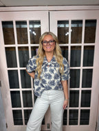 A woman wearing the Dawn Blouse Featuring a floral jacquard woven fabric, puff shoulders, a classic button-down front, and a delicate tie-neck detail