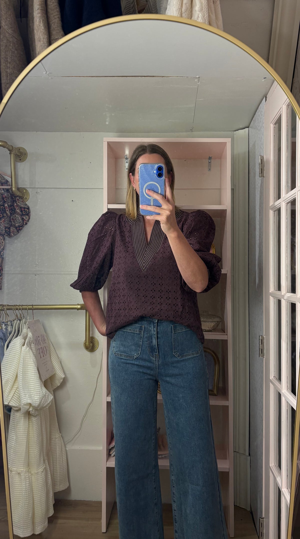 A woman takes a mirror selfie in a fitting room wearing a chocolate  textured puff-sleeve blouse and blue wide-leg jeans.
