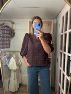 A woman takes a mirror selfie in a room showing a chocolate eyelet puff-sleeve blouse with a V-neck, paired with blue jeans.