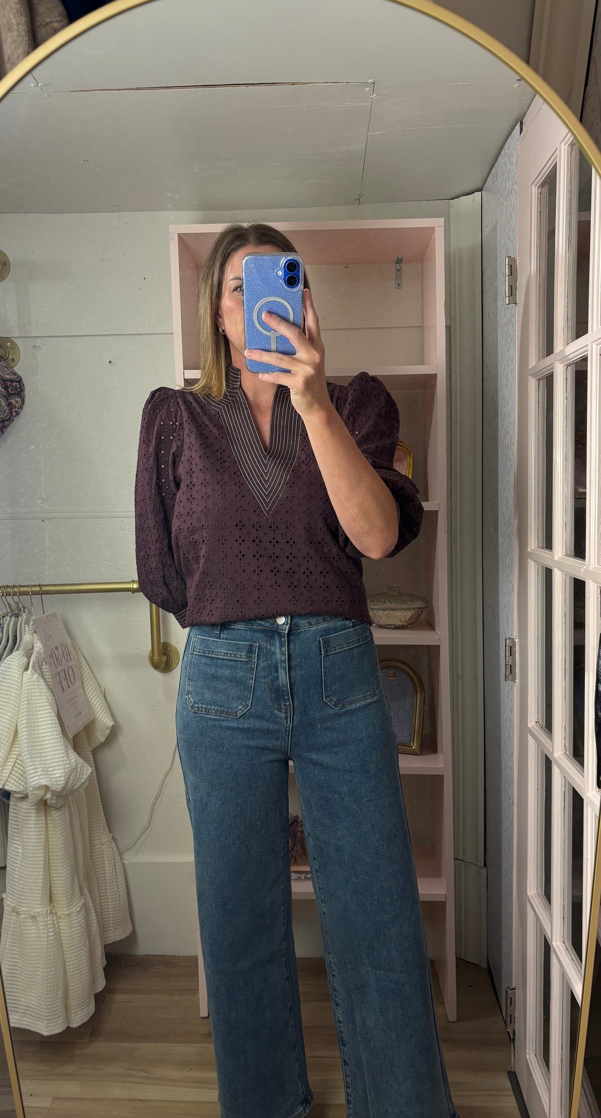 A woman takes a mirror selfie in a room, wearing a dark purple textured puff-sleeve top and blue wide-leg jeans.