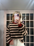 A person taking a mirror selfie wearing a fuzzy knit sweater with horizontal black and beige stripes, featuring a contrasting red crew neck and cuffs, paired with white pants.
