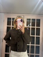 A woman takes a mirror selfie wearing a dark brown knit button-up cardigan sweater and white pants, standing in front of a pink glass-paneled door.