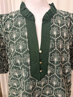 A dark green blouse with a white floral and chain pattern, featuring a ruffled mock neck and a buttoned front placket, displayed on a mannequin.
